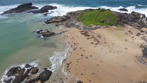 Schaumige-Wellen,-Die-Auf-Einer-Grünen-Landzunge-Mit-Felsvorsprüngen-In-Der-Nähe-Der-Landzunge-Von-Bonville-Am-Strand-Von-Sawtell-In-New-South-Wales,-Australien,-Spritzen