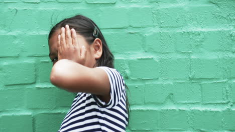 A young biracial girl with long black hair stands before green background, copy space