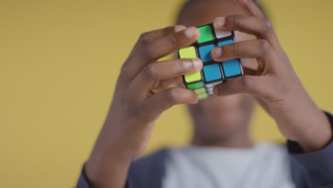 retrato de estudio de un niño en el espectro asd resolviendo un cubo de rompecabezas sobre fondo amarillo 5