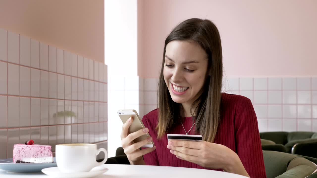 mujer hermosa comprando en línea con tarjeta de crédito usando teléfono inteligente en casa. estilo de vida. chica bonita mirando a la cámara y sonriendo. aplicación bancaria conectada. mujer con teléfono y tarjeta bancaria en el interior. 60 fps
