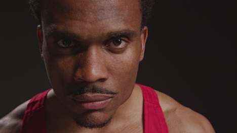 Close-Up-Portrait-Of-Serious-Male-Boxer-Wearing-Vest-Walking-Towards-Camera-And-Into-Focus-Training-For-Sports-Event-Against-Black-Studio-Background