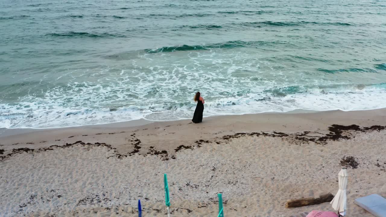 손에 와인 한 잔과 머리카락에 바람을 들고 해변을 고 있는 소녀의 공중 풍경