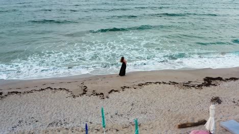 Luftaufnahme-Eines-Mädchens,-Das-Mit-Einem-Glas-Wein-In-Der-Hand-Und-Dem-Wind-Im-Haar-Am-Strand-Entlang-Geht