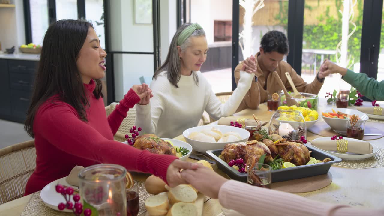 Extended family gathering at home with turkeys on table, holding hands feeling grateful for prayer