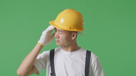 close up of asian man painter wearing safety helmet having a headache while standing in the green screen background studio