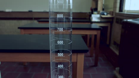 Levantando-A-Lo-Largo-De-Un-Cilindro-Graduado-De-1000-Ml-En-Un-Banco-De-Laboratorio-Negro-En-Un-Laboratorio-De-Química-De-La-Escuela-Secundaria