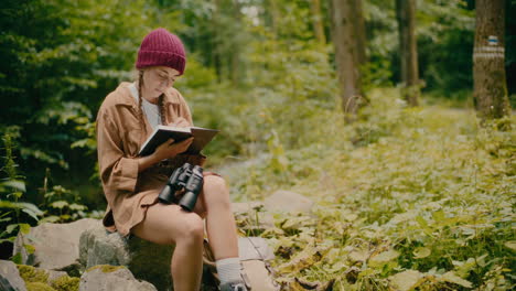 Frau-Schreibt-In-Einem-Buch-Und-Sitzt-Auf-Einem-Felsen-Im-Wald