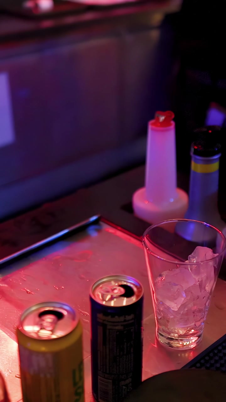 Barman prepara un cocktail con ghiaccio, lattine di energy drink e shaker sotto un'illuminazione al neon colorata