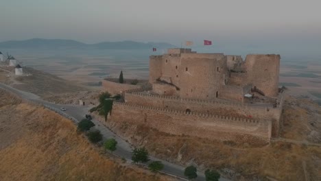 Aerial-shot-of-Consuegra-castle,-in-Spain,-with-a-row-of-windmills-at-background