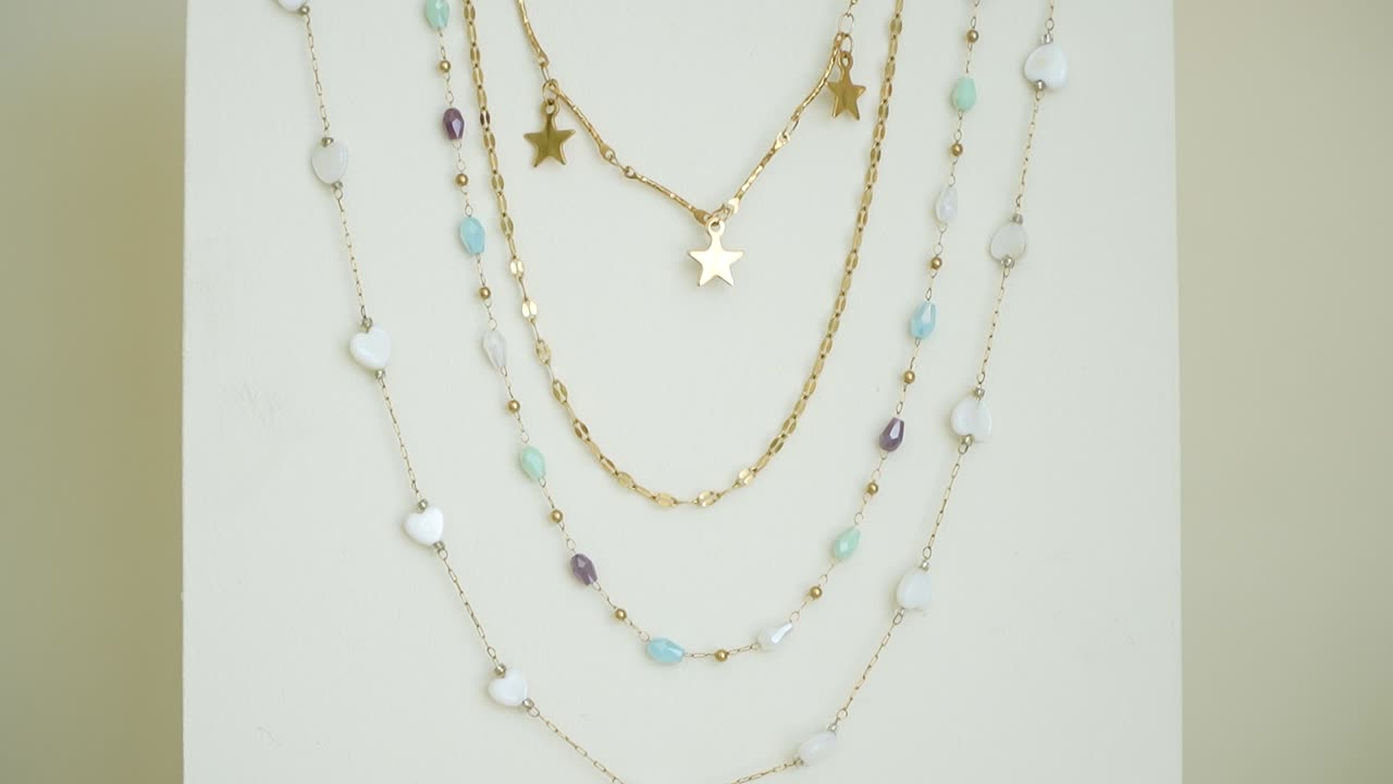 Layered necklaces with delicate stars and colorful gemstones are beautifully arranged on a neutral backdrop. The elegant designs highlight unique textures and colors, perfect for any outfit