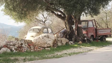 Alter-Volkswagenkäfer-Und-Ein-Alter-Pick-up-lastwagen,-Der-Unter-Einem-Olivenbaum,-Griechenland,-Aufgegeben-Wurde