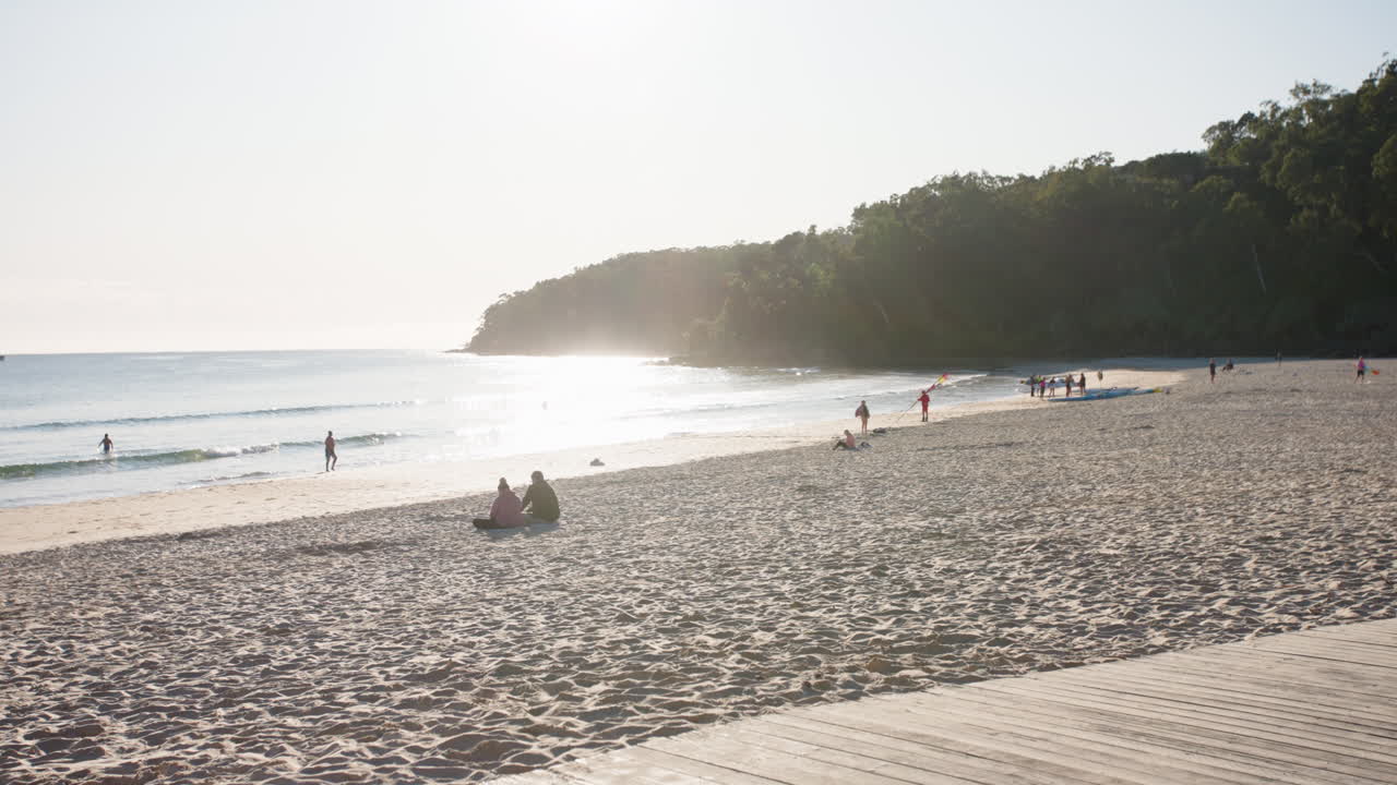 romántica playa escénica con la luz del sol de la tarde reflejándose en el océano y la gente en la playa de arena, cámara lenta de 4k