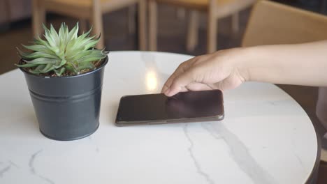 a woman's hand reaches for her smartphone on a table in a cafe