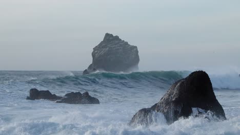 rugged wild basalt rock formation with large waves breaking on shore, mysterious scene