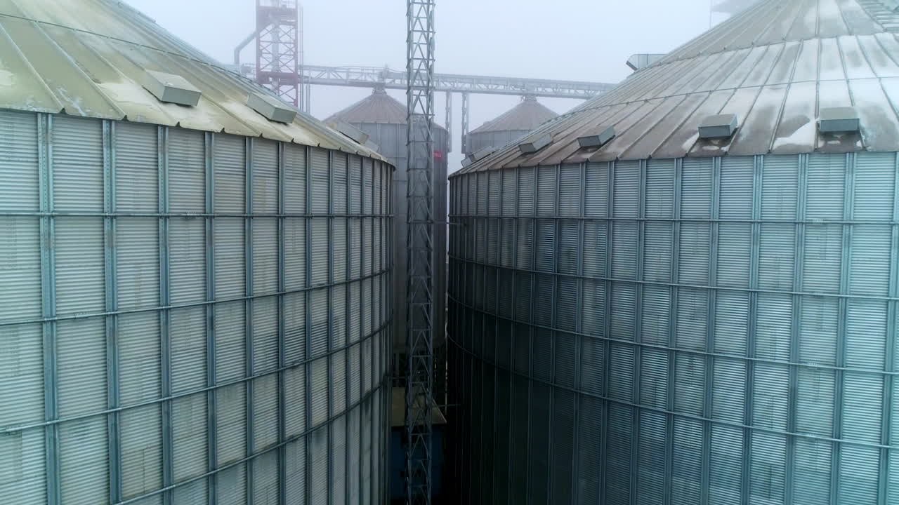 Massive tanks of elevator storage factory. Metal exterior of huge granary complexes on foggy day. Support between the containers.