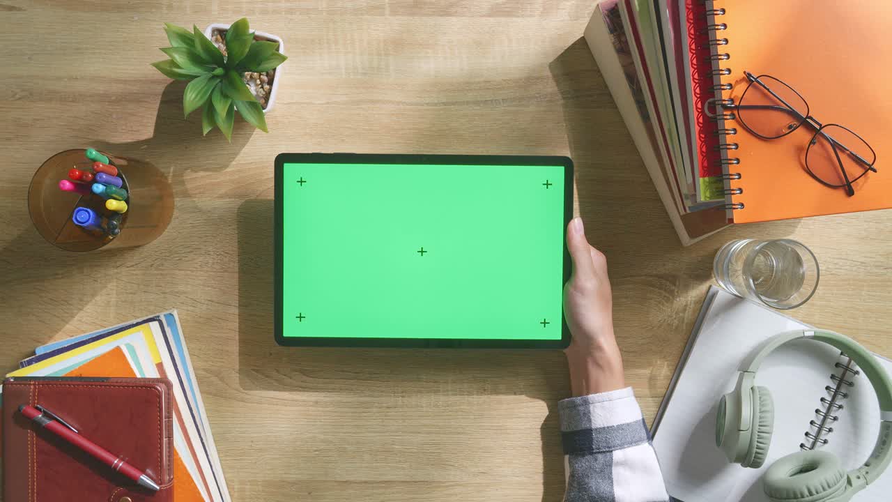 vista de arriba hacia abajo de una computadora portátil con pantalla verde simulada pantalla chromakey en un escritorio de oficina de madera al lado de la libreta con bolígrafos, gafas y un vaso de agua.