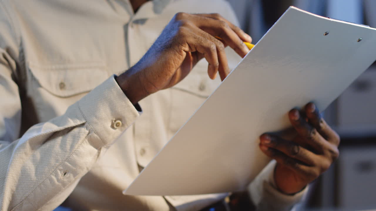 Close Up View Of Office Worker Sitting At Desk And Checking Some Documents With A Pencil In A Hand In The Office At Night