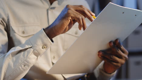 close up view of office worker sitting at desk and checking some documents with a pencil in a hand in the office at night