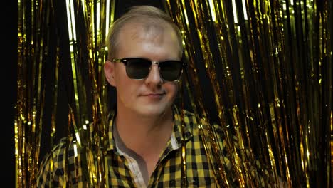 Portrait-of-caucasian-man-posing-on-black-background.-Gold-shining-foil-strips.-Party,-music,-disco