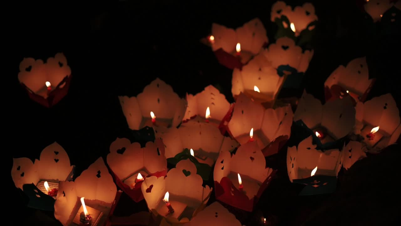 Lanterne che brillano soffusamente. Festività notturne con lanterne luminose e decorazioni di loto galleggianti. Scena celebrativa con lanterne di carta luminose sull'acqua tra loti in fiore e un'atmosfera festosa.