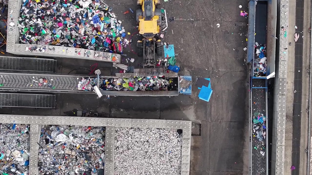 Plastic waste is sorted and processed in a recycling facility. Heavy machinery moves materials for recovery. Various types of plastic waste are collected for processing.