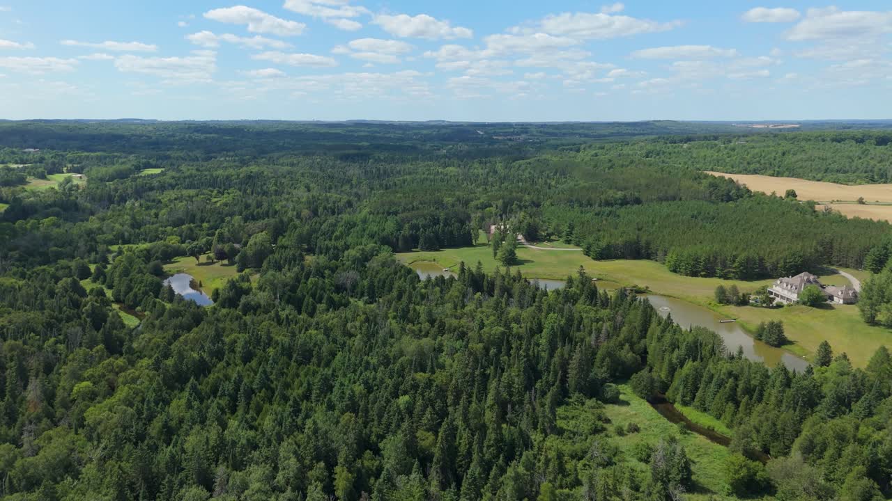 Drone flyover of trout fishing club surrounded by dense forest and fields in rural countryside