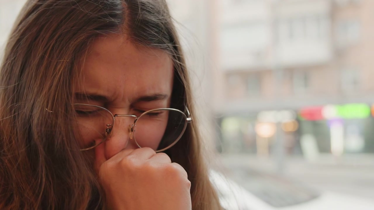 Closeup of woman crying in city scene. Woman wiping tears with trembling hands in urban setting. Raw emotional release captured as distressed woman mourns in bustling city background
