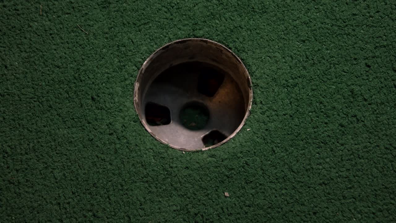 una vista de pájaro de cerca de una mini pelota de golf amarilla cae en el hoyo de golf y rebota en el bolsillo en un campo