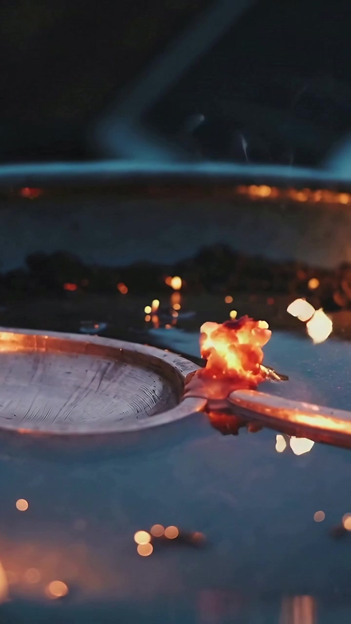Vertical video: Moving molten blob leaving trail on handle to pan rim at bench with sparks falling
