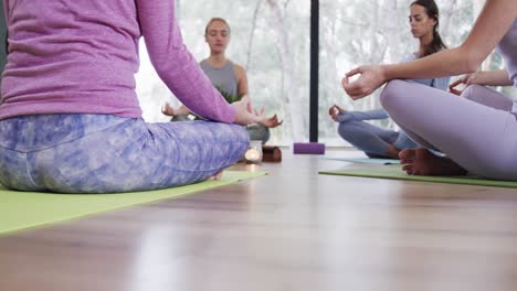 diverse women meditating in lotus pose while sitting on mats in yoga studio