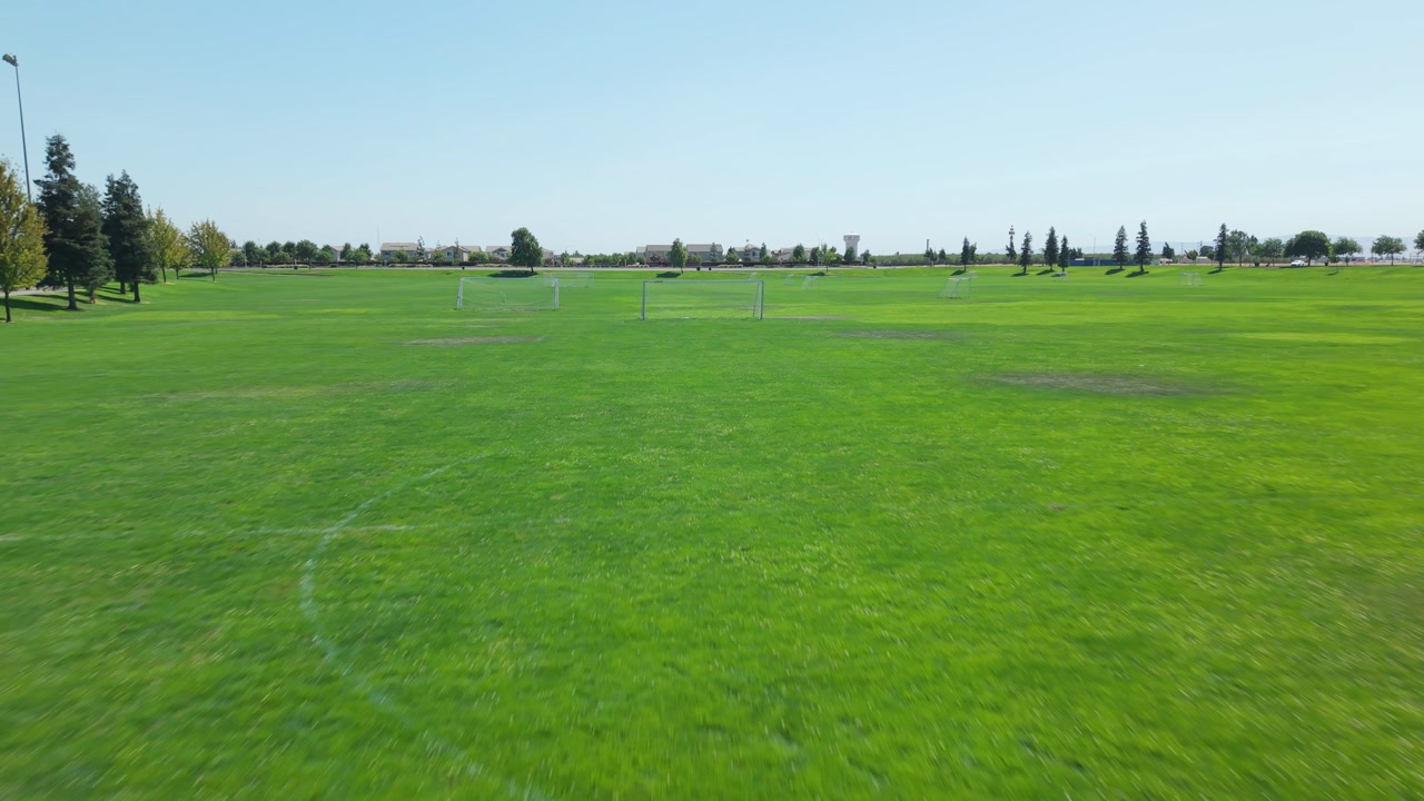 Low drone shot moving backward across soccer goals on green field.