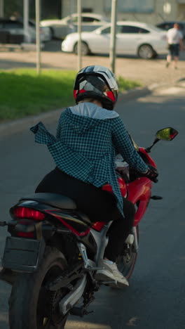 un jinete en una bicicleta eléctrica roja cruzando a lo largo de una carretera urbana serena, el jinete está usando una camisa a cuadros y un casco, dirigiéndose hacia un cruce de peatones con peatones en la distancia