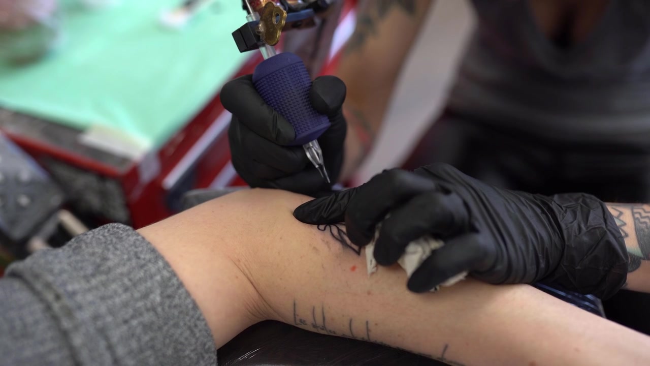 Tatuatrice che tatua una pesca sul braccio di una donna