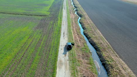 Rotating-aerial-shot-of-a-man-standing-next-to-a-car-on-an-empty-rural-road-in-the-farmlands-of-Cresnjevec,-Slovenia