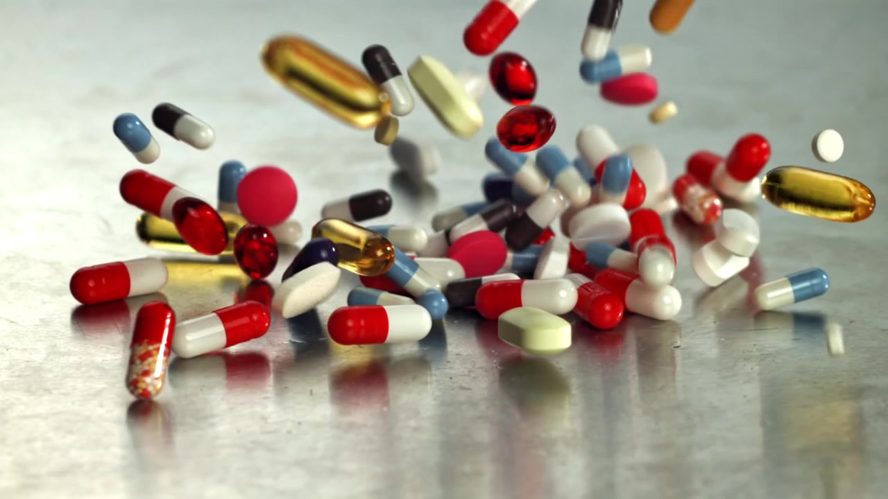 Various Colorful Pills and Capsules Falling onto a Metallic Surface in Slow Motion