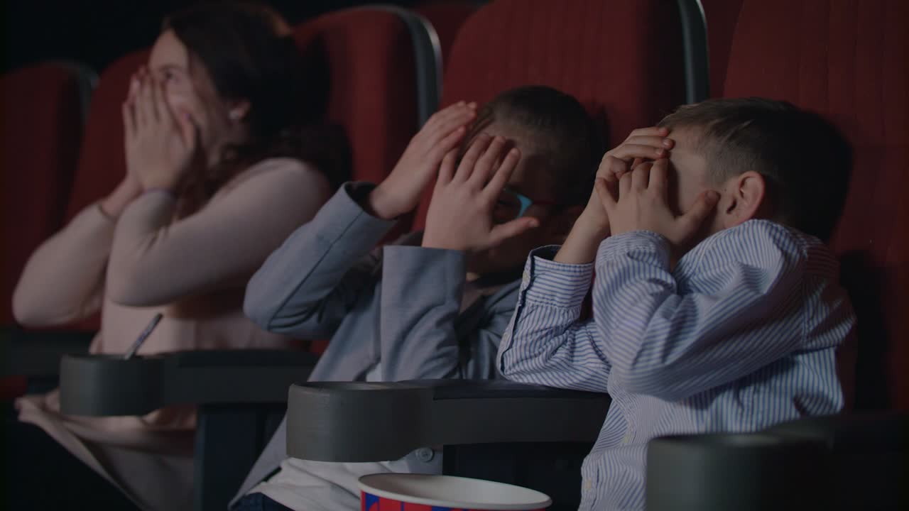 los niños se asustan en el cine. los niños asustados se cubren la cara con las manos.