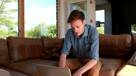 un joven guapo relajándose en su sofá usando una computadora portátil