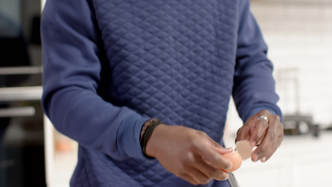 Cracking egg, person in blue sweater preparing food in kitchen