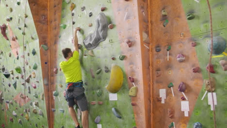 climber getting geared up with harness lead rope chalk bag carabiner and belay. man climber climbs the wall with a rope to the top