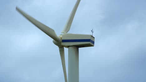 wind turbine rotating against grey cloudy sky closeup from rear side