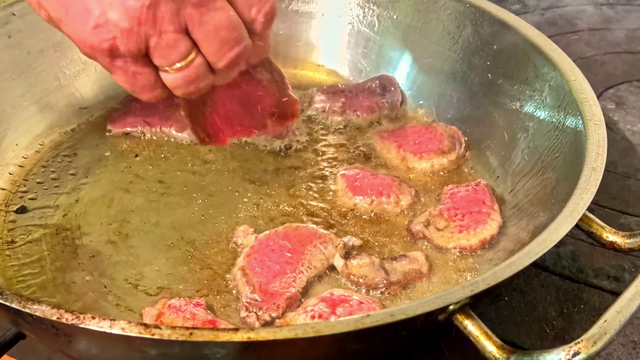 Beef medallions frying in hot oil, preparing a delicious steak dinner in metal pan