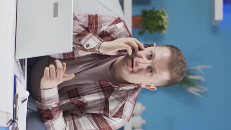 Vertical-video-of-Home-office-worker-man-talking-on-the-phone-happily.