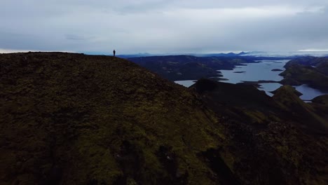 aerial drone landscape view of a silhouette of one person, standing on top of a mountain, in the iceland highlands