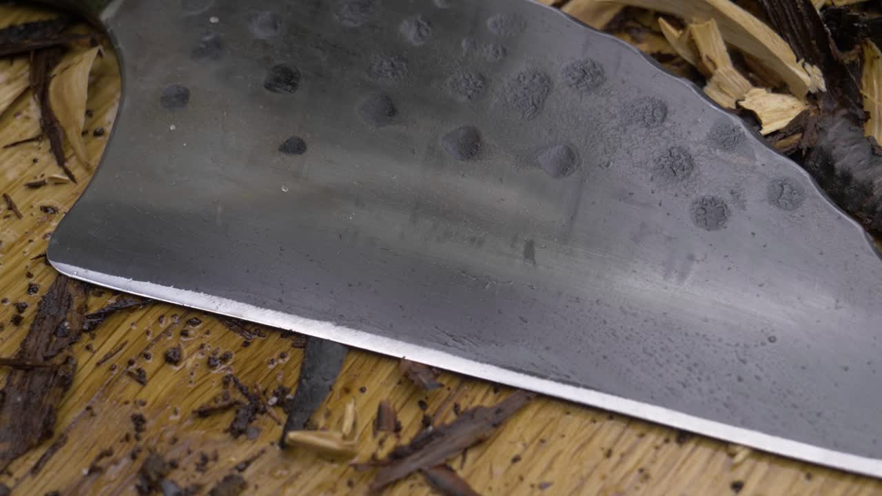 Traditional chef's knife, made very sharp by hand, pours piles of salt and pepper very slowly over it. The kitchen knife is in nature on a wooden chopper