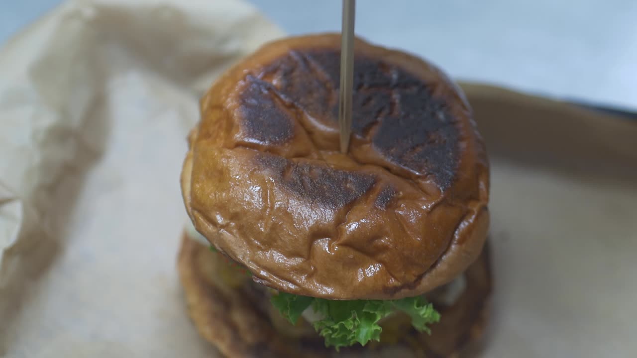 se coloca un palillo grande en la parte superior de una hamburguesa gourmet en un restaurante como toque final.