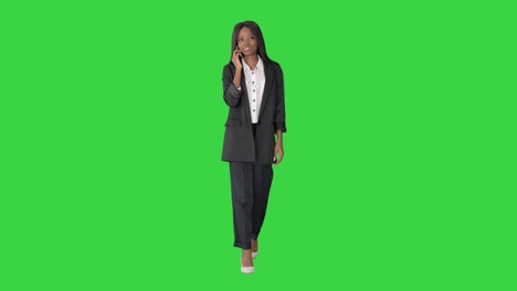 casual african american businesswoman talking on phone while walking on a green screen, chroma key