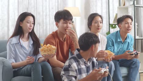 asian teenagers eating and playing video games at home.