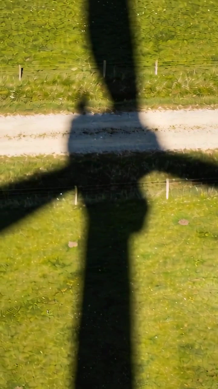 Pystysuuntainen video: Pyörivän tornin varjo pyyhkii aurinkoista peltoa, tuuli pyörittää napaa ja lapoja sähköntuotantoa varten.