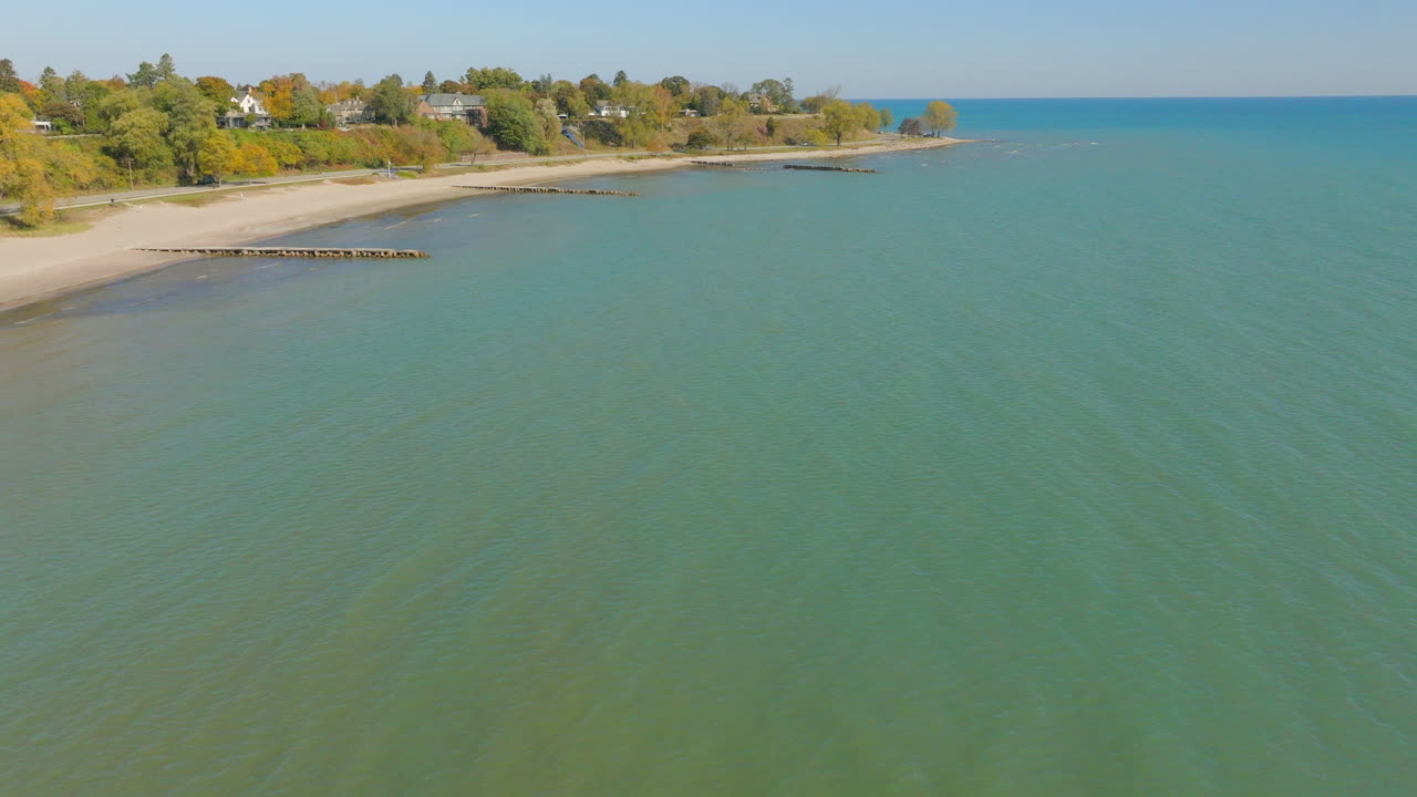 Drone aerial over bright blue water of Lake Michigan on a pretty autumn day toward the Sheboygan, Wisconsin shoreline with colorful trees and charming neighborhood houses
