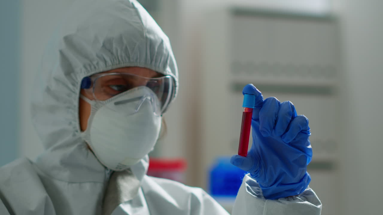 Biochimico in tuta protettiva che tiene un campione di sangue e analizza una reazione chimica